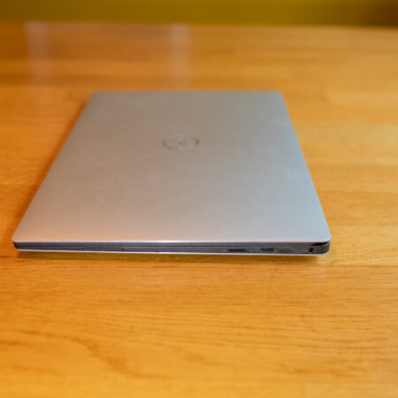 Closed silver laptop resting on a wooden table, showing side ports.