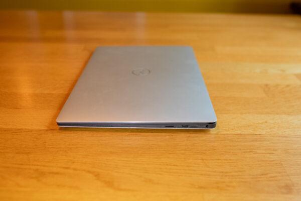 Closed silver laptop resting on a wooden table, showing side ports.