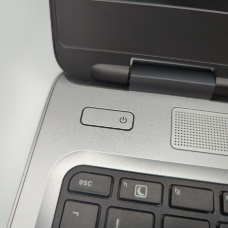 Close-up of a laptop's power button and keyboard corner, featuring the edge of a speaker grille.