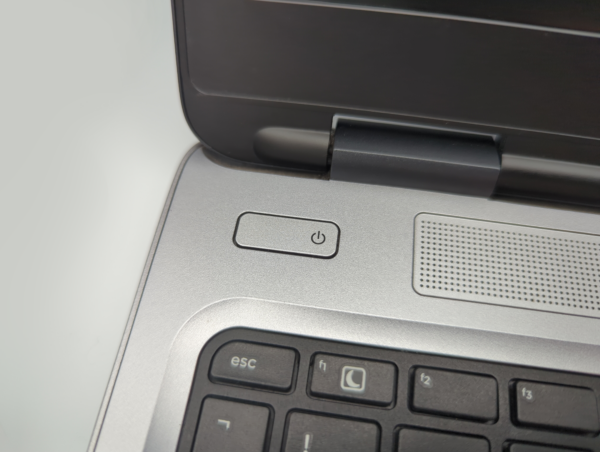 Close-up of a laptop's power button and keyboard corner, featuring the edge of a speaker grille.