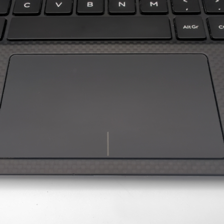 Laptop touchpad and keyboard close-up with a textured carbon fiber finish.