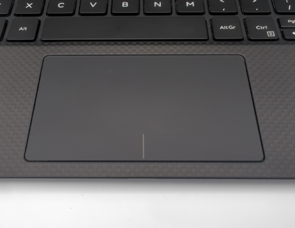 Laptop touchpad and keyboard close-up with a textured carbon fiber finish.
