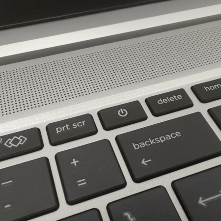 Close-up of a laptop keyboard showing power, delete, and backspace keys with a speaker grille in the background.