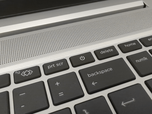 Close-up of a laptop keyboard showing power, delete, and backspace keys with a speaker grille in the background.