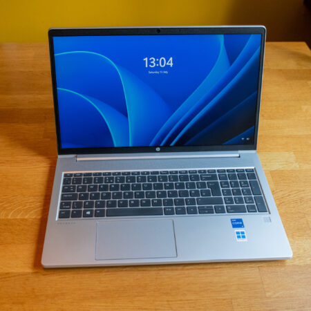 Silver laptop on wooden desk with a blue screen display showing the time as 13:04, featuring Windows and Intel Core stickers.