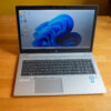 Laptop with Windows 11 desktop, placed on wooden table, displaying blue swirl wallpaper.