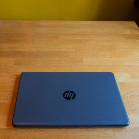 Closed HP laptop on a wooden table, against a yellow wall.