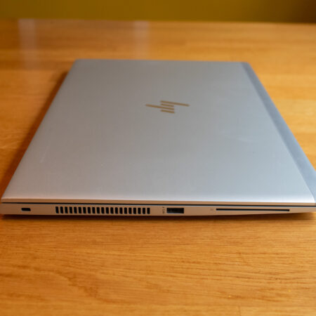 Silver laptop closed on a wooden table, showing side ports and sleek design. Ideal for modern workspace.
