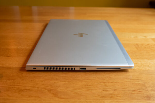 Silver laptop closed on a wooden table, showing side ports and sleek design. Ideal for modern workspace.