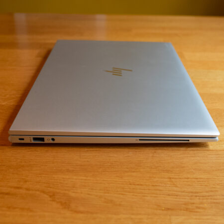 Closed silver laptop on a wooden table, showcasing side ports and sleek design.