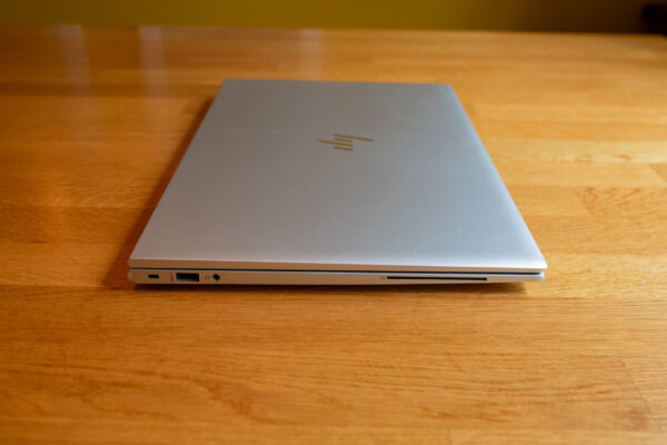 Closed silver laptop on a wooden table, showcasing side ports and sleek design.