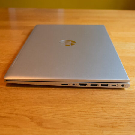 Closed silver laptop on a wooden table showcasing side ports, including USB and HDMI connections.