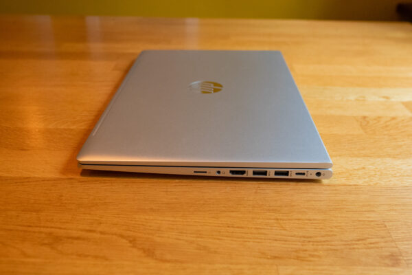 Closed silver laptop on a wooden table showcasing side ports, including USB and HDMI connections.