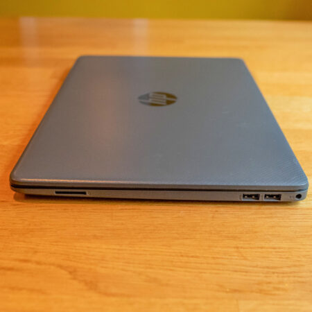 Closed laptop on wooden table showing USB ports and SD card slot.