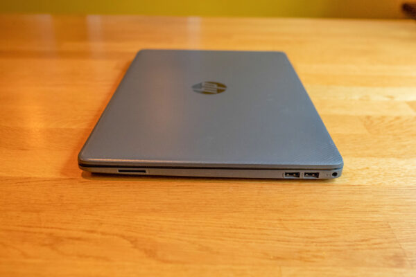 Closed laptop on wooden table showing USB ports and SD card slot.