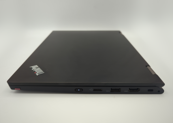 Closed black laptop with visible brand logo, showing multiple port connections on the side, on a white surface.