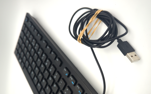 Black keyboard with a coiled USB cable secured with a rubber band on a white background.